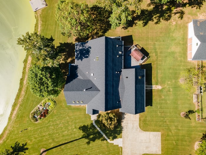 top-down view of a country house with a grey roof next to a pond and large green lawn.
